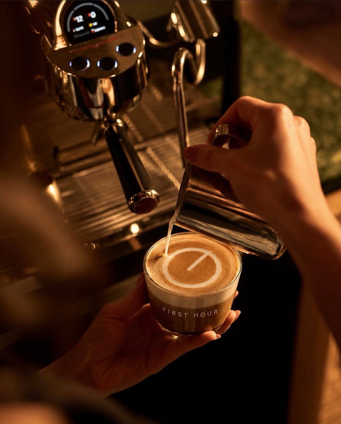 Latte being poured into a First Hour cup under an espresso machine.